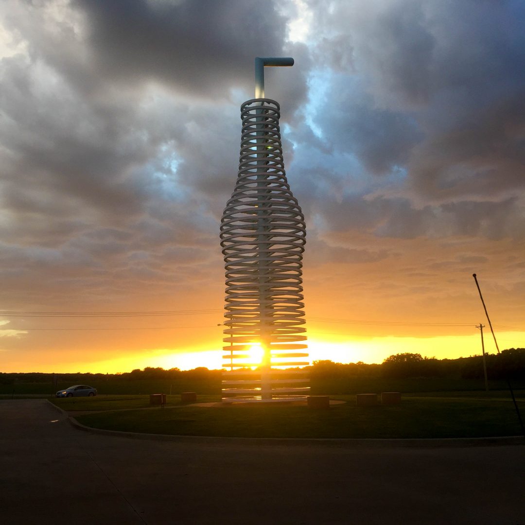 the sun shining through a giant soda bottle statue