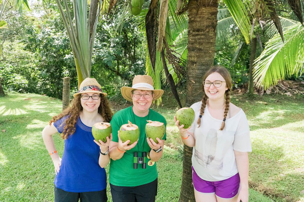 Isabel, Linda, and Addie holding coconuts under a palm tree