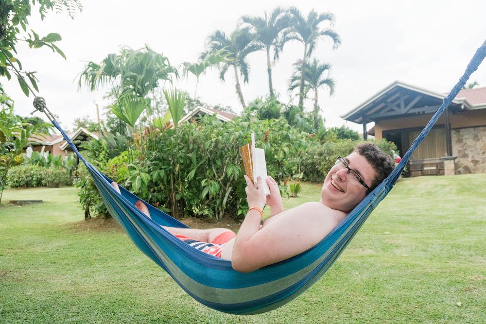 Daniel reading a book and smiling in a hammock