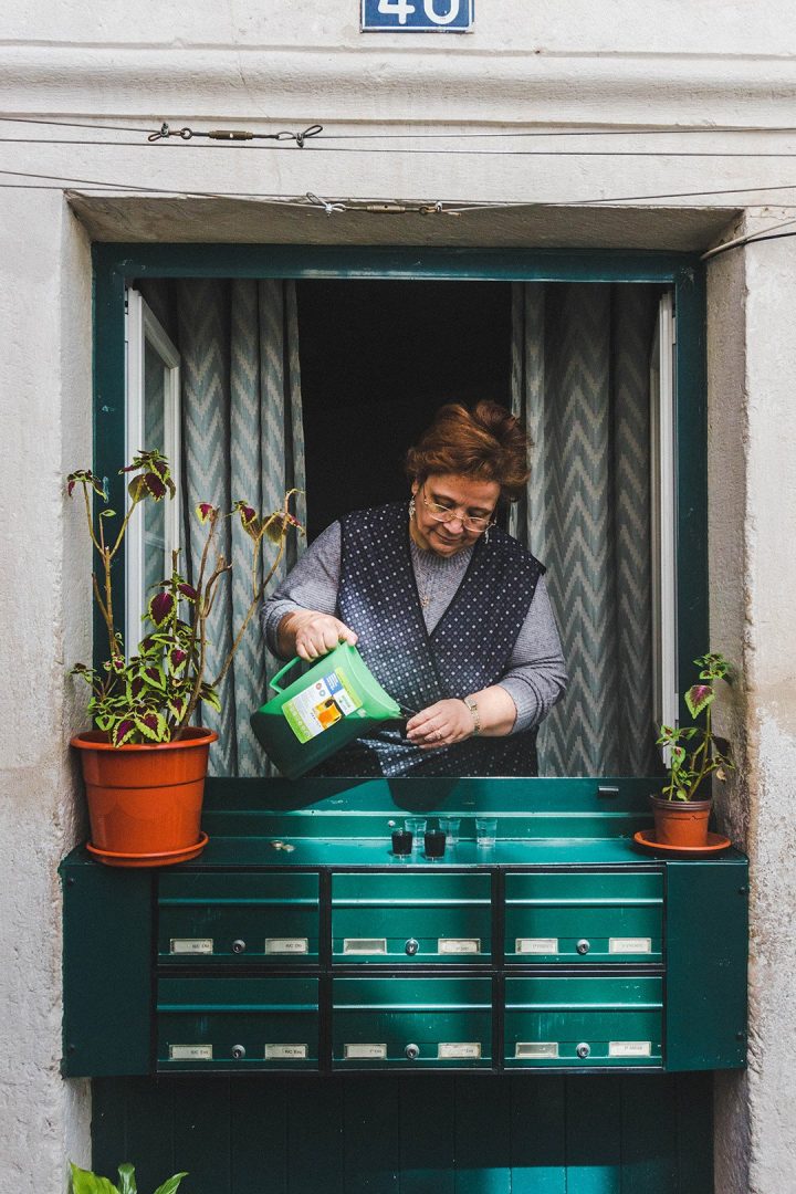 A middle-aged woman named Tininna leaning out a window and pouring ginjinha in Lisbon, Portugal