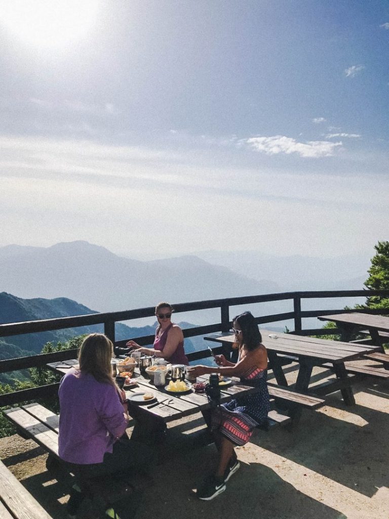 Girls eating breakfast at a picnic table overlooking some mountains