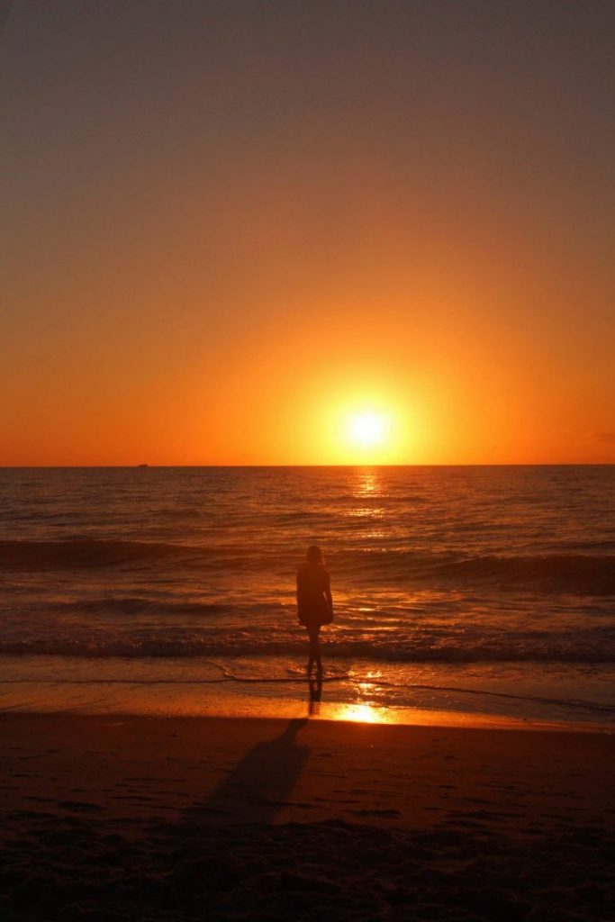 A girl silhouetted by sunset on a beach