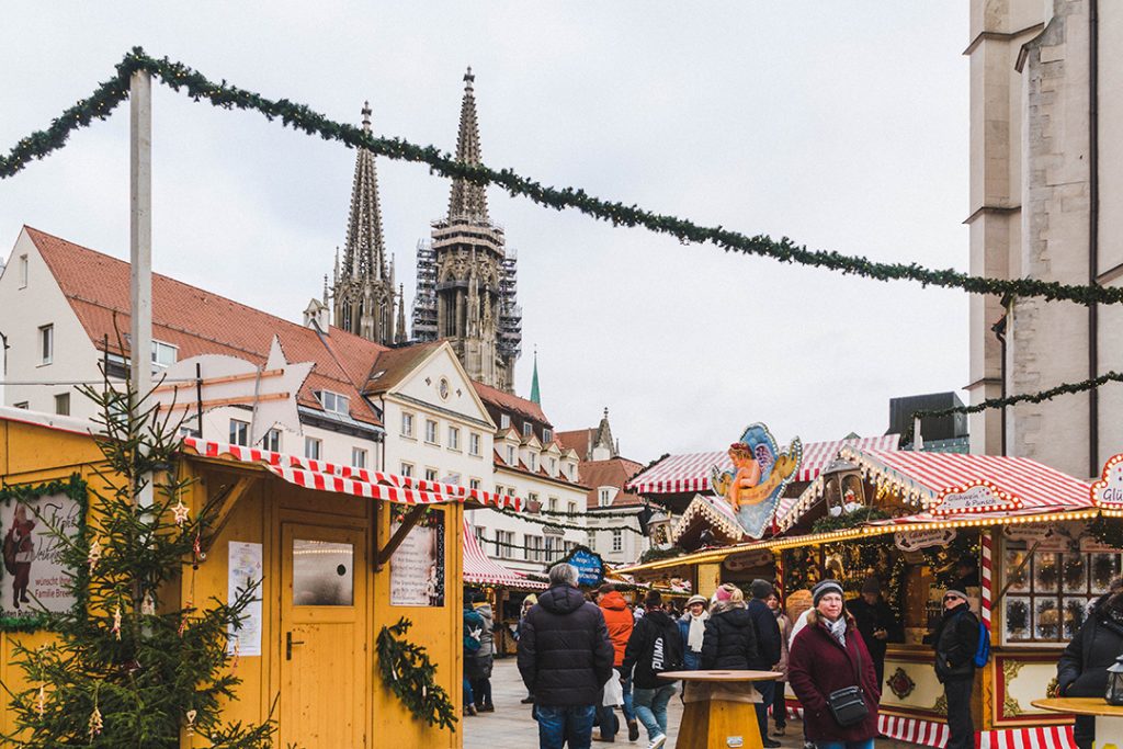 Small wooden booths line a square which a gothic church overlooks at the Regensburg Christmas Market