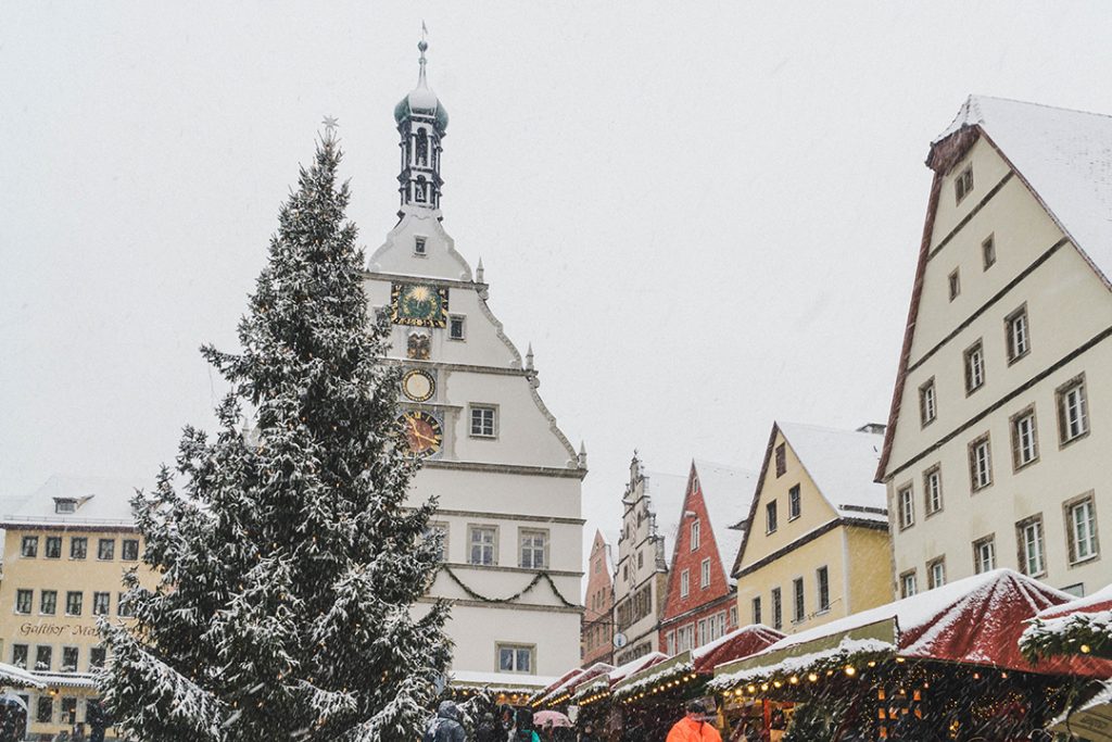 a large evergreen tree covered in snow in a colorful square at the Rothenburg ob der Tauber Christmas Market
