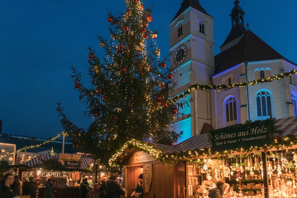 small wooden booths and a large christmas tree lit up at night