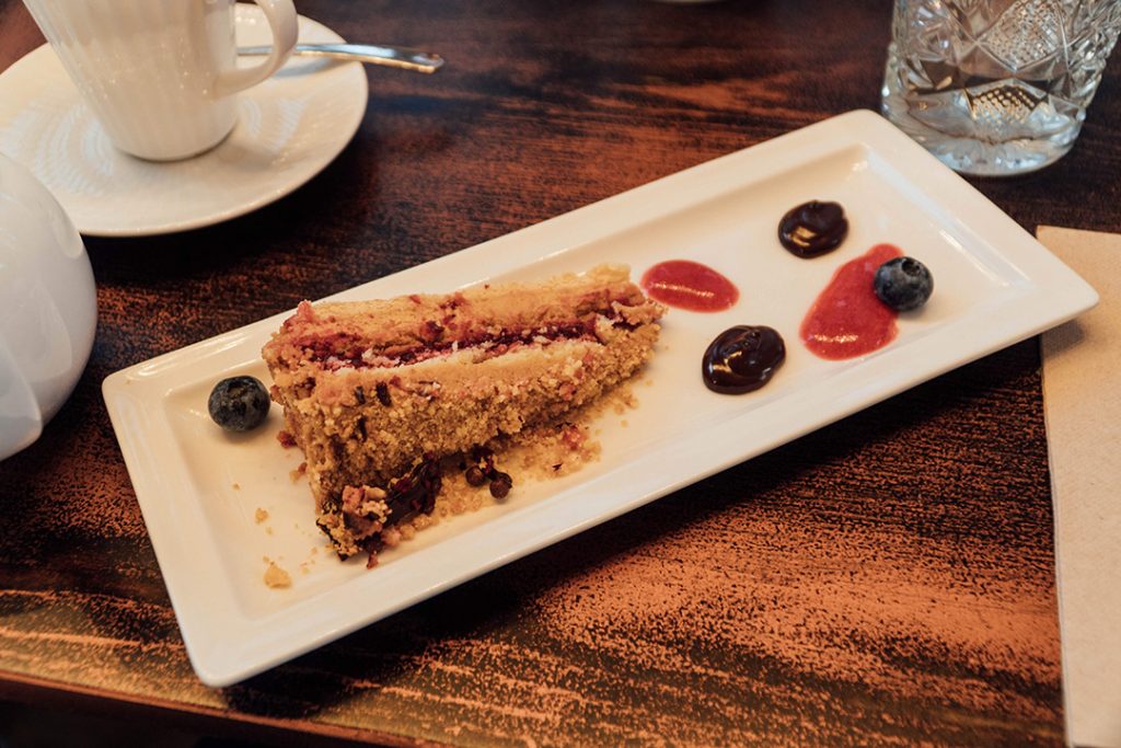 a slice of cranberry and caramel cake on a plate with several wells of sauce