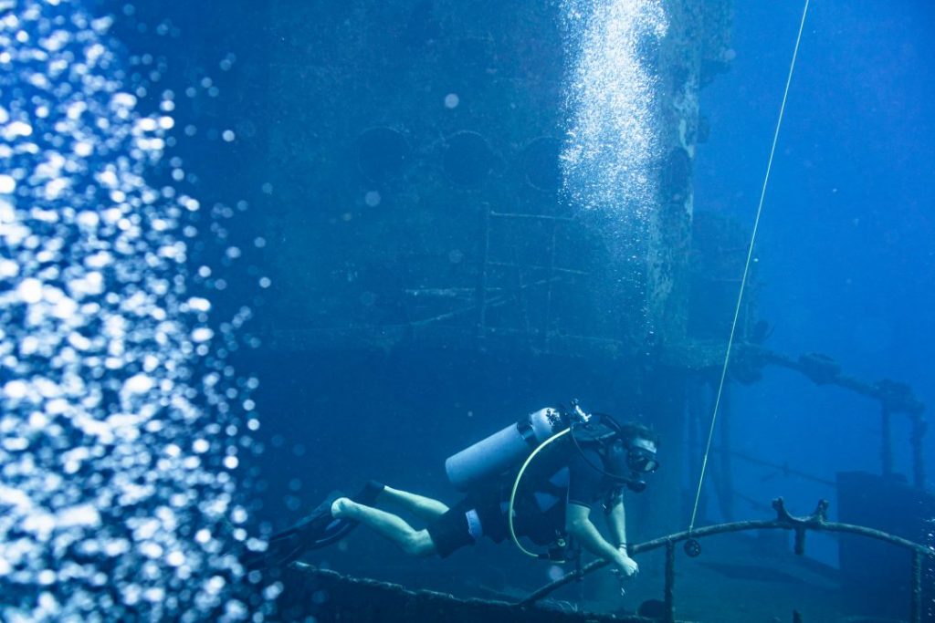 a scuba diver diving in front of a ship wreck
