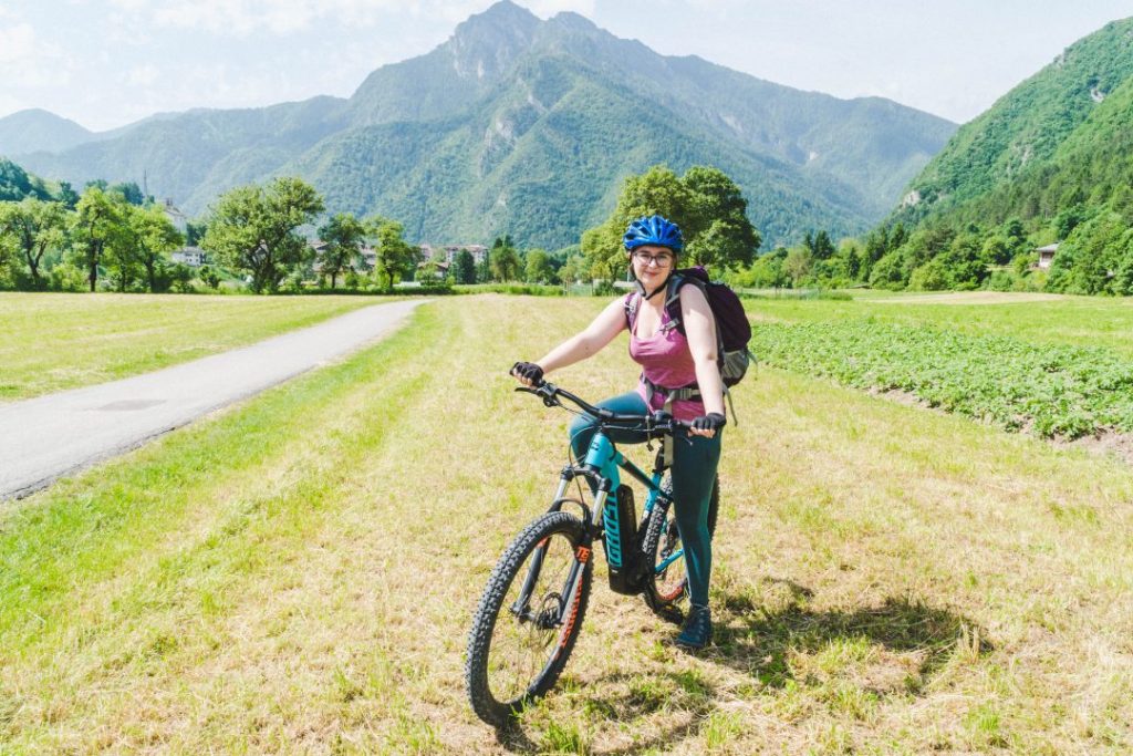 Addie smiling confidently on a mountain bike in front of a mountain in Valle di Ledro, Italy