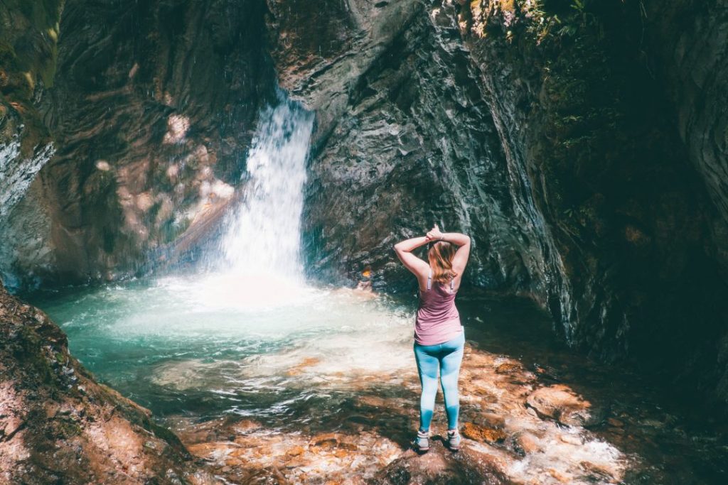 Addie standing with her hands over her head in front of a small, illuminated waterfall