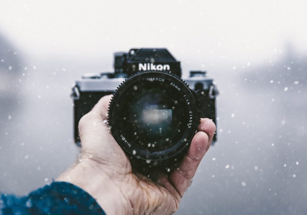 A hand holding a Nikon camera in the snow - how to choose the best camera for travel photography