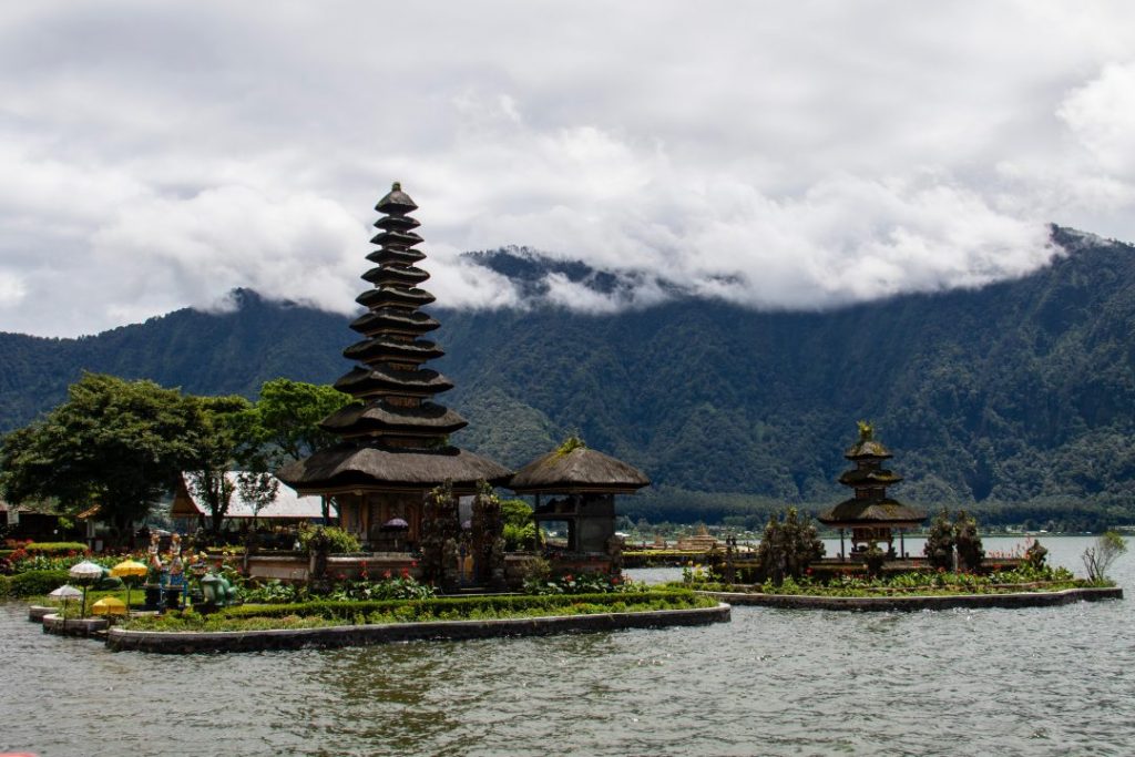 tiered bali temple on a lake with mountains in the background