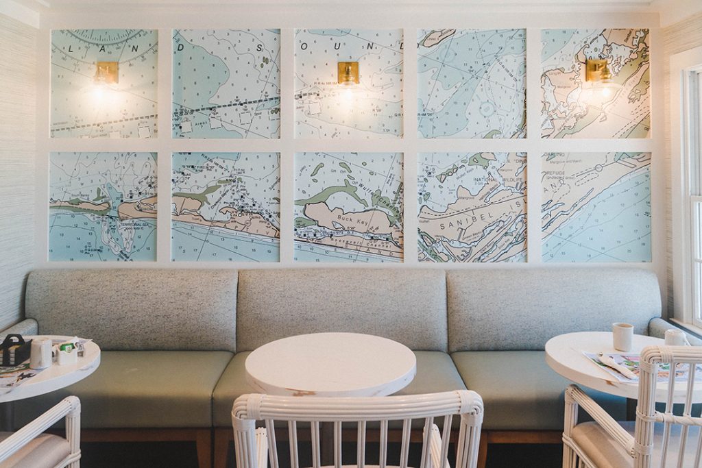 a little nook with a grey couch, white tables and chairs and a blue map of captiva island on the wall