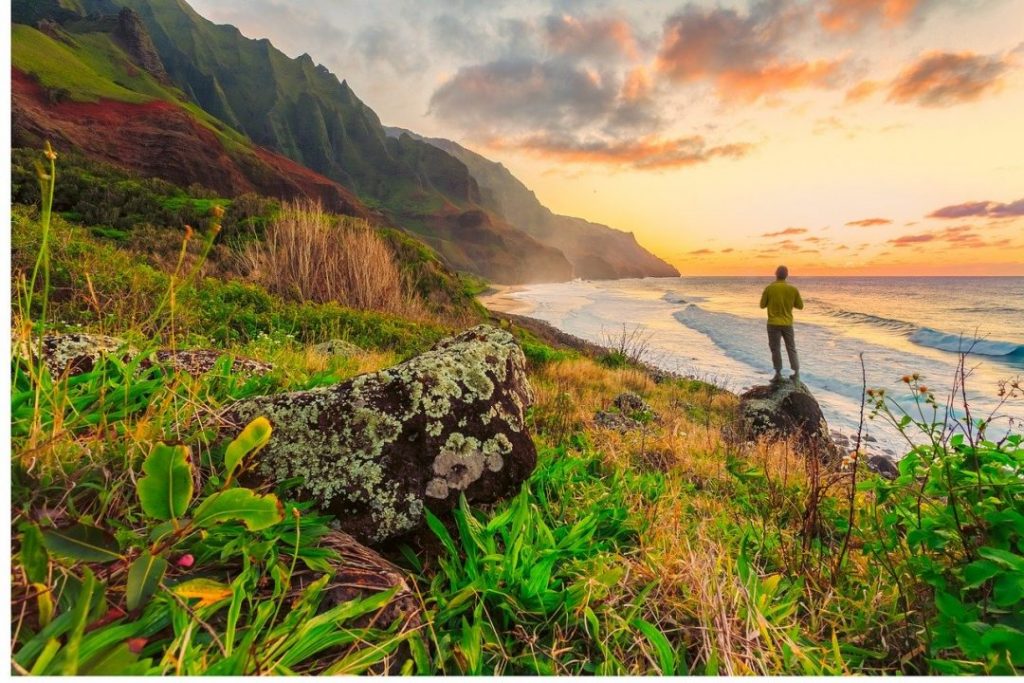 a man standing on a rock in front of a rocky coastline at sunset in Oahu, Hawaii, one of the best spring break destinations in the us