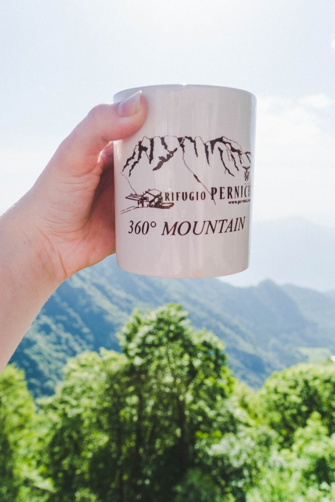 hand holding up a rifugio pernici mug in front of a mountain background