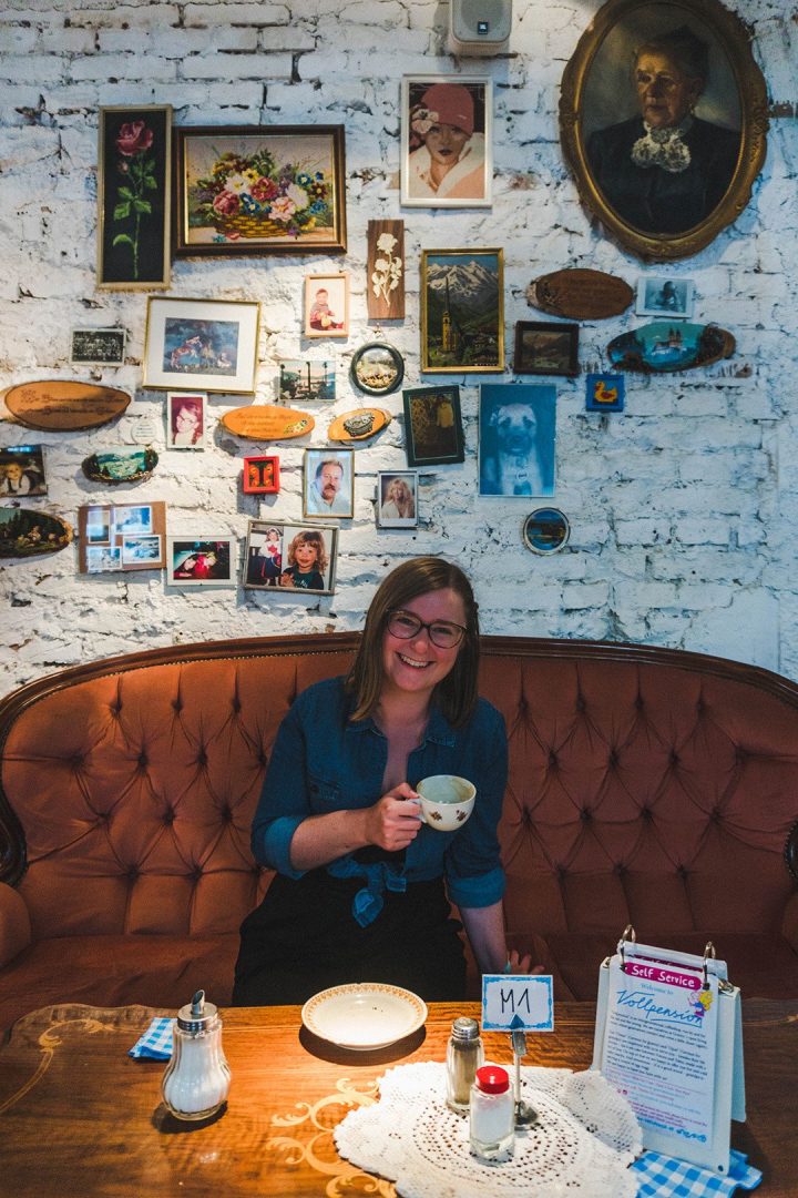 Addie with coffee in front of a wall of photographs at Cafe Vollpension in Vienna, Austria