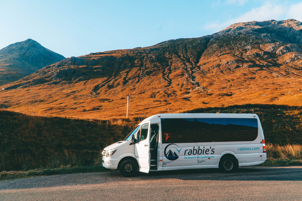 A Rabbie's minivan against a stunning highland hill on its isle of skye tour from edinburgh