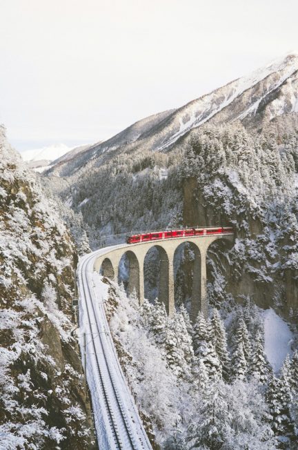 a train going over a viaduct in a snowy mountain landscape