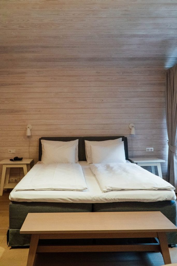 a bed with white bedding against a wood plank wall