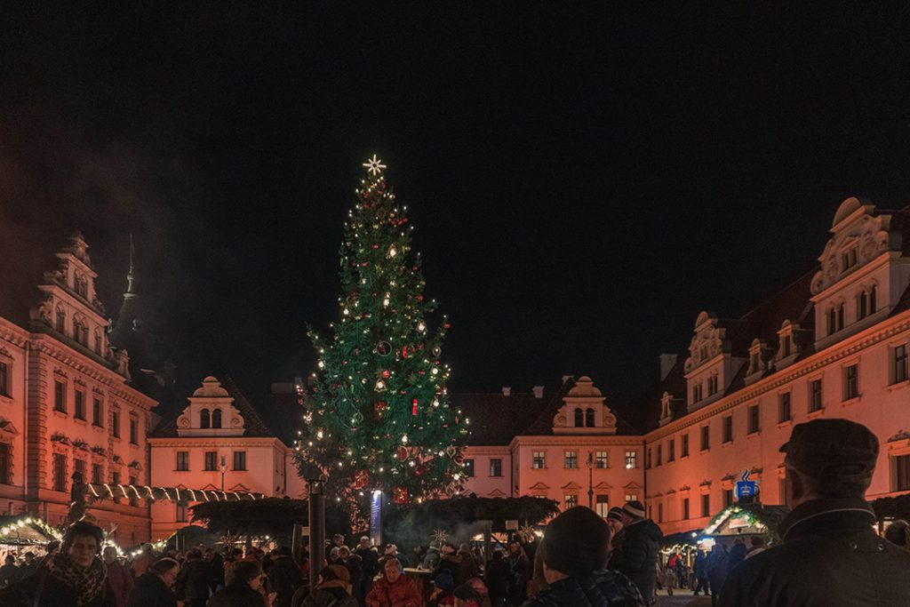 a huge christmas tree towers over small wooden booths in a castle courtyard