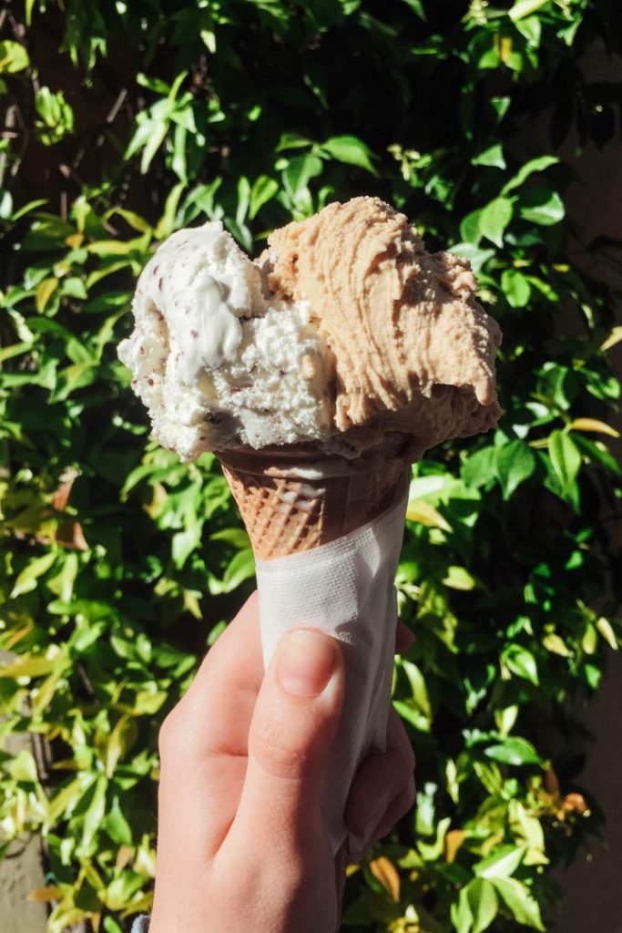 a hand holding up a cone full of gelato against an ivy wall. don't make a common rome travel mistake and get gelato from a piled high tub
