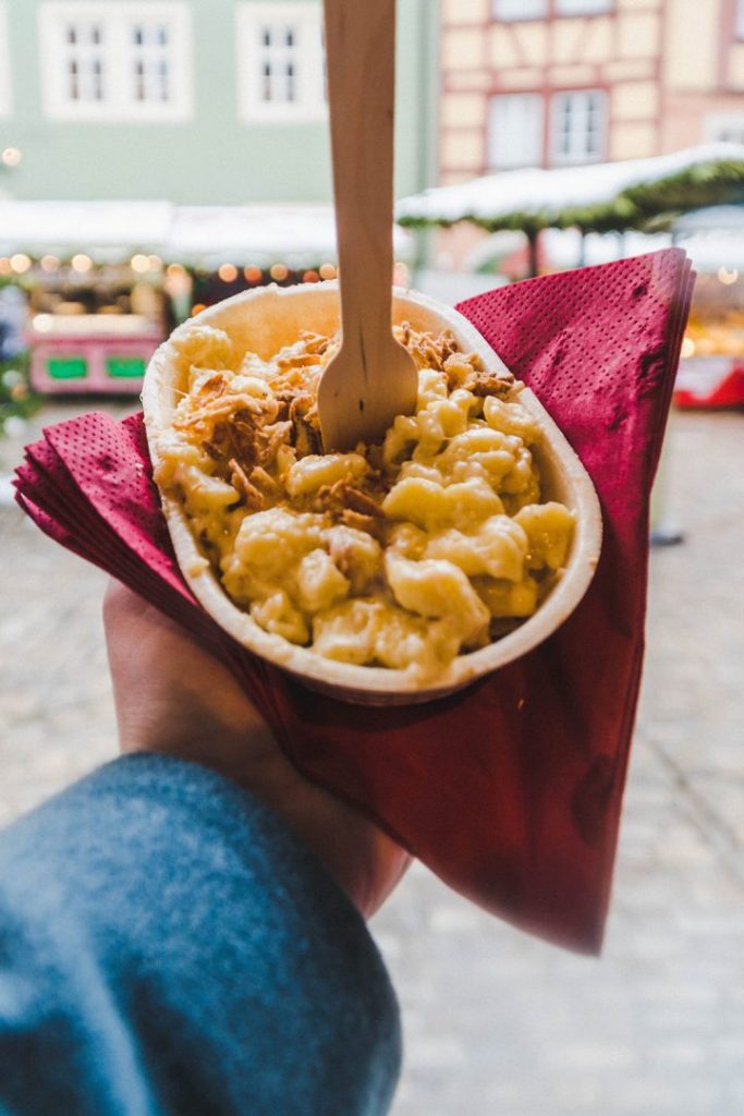 A hand holding up a small dish of extremely cheesy egg noodles - käsespätzle at the Rothenburg ob der Tauber Christmas Market