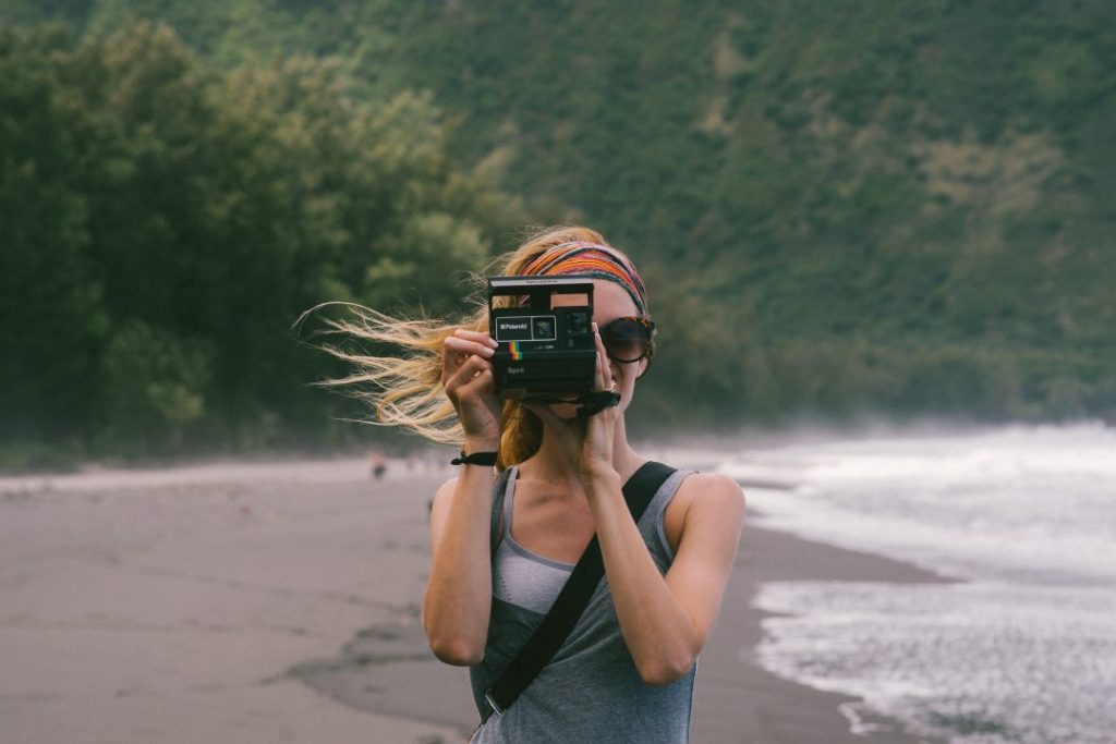 A woman by the ocean, holding a camera up to her face