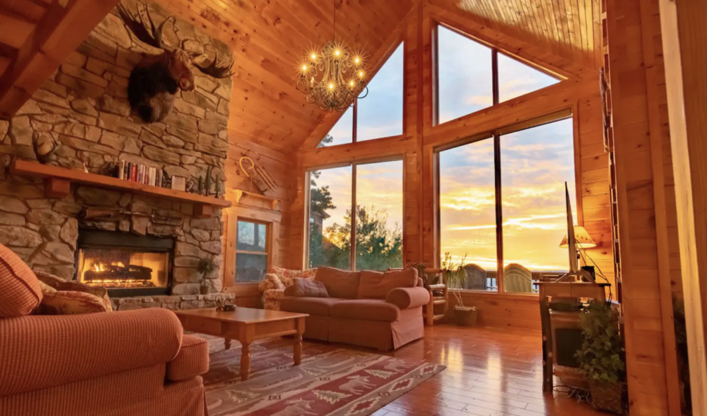 a living room with comfortable couches, a stone fireplace, and floor-to-ceiling windows with a view of the sunset